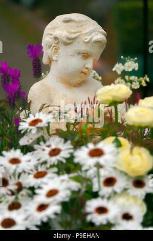 Kleine Engel in einem BLUMENGARTEN. Skulptur eines niedlichen kleinen Engel in einem Garten mit Sortiment an blühenden Sorten. Stockfoto