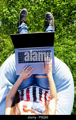 Ansicht von oben. Frau auf dem Laptop Computer mit leeren schwarzen leeren Bildschirm Platz im Park auf grünem Gras Sonne Rasen im Freien zu kopieren. Stockfoto