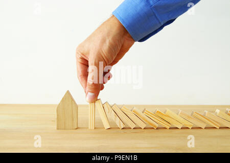 Konzept Bild von Immobilien Versicherungen und Schutz. Mann die Hände die Blockierung der Domino Effekt zu speichern, ein kleines Haus Stockfoto
