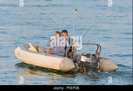 Zwei Männer in einer Rippe mit einem Außenbordmotor auf dem Wasser am Abend im Sommer in Großbritannien. Stockfoto