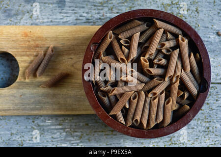 Hohe Betrachtungswinkel und eine hölzerne Schüssel voller roher Buchweizen Penne auf einem grauen rustikalen Holztisch rigate Stockfoto