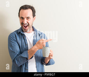 Ältere Menschen trinken Kaffee in einem Becher sehr zufrieden zeigt mit Finger- und an der Seite Stockfoto