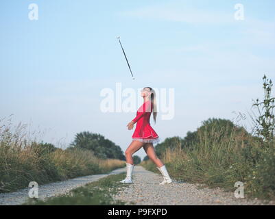 Bebrillter blonder Teen Majorette Mädchen Twirling Baton draußen im roten Kleid Stockfoto