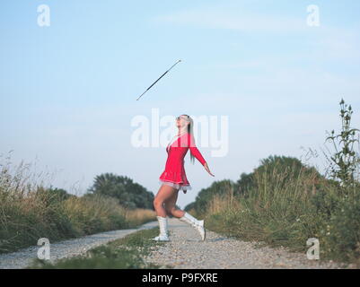 Bebrillter blonder Teen Majorette Mädchen Twirling Baton draußen im roten Kleid Stockfoto