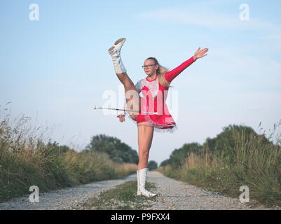 Bebrillter blonder Teen Majorette Mädchen Twirling Baton draußen im roten Kleid Stockfoto