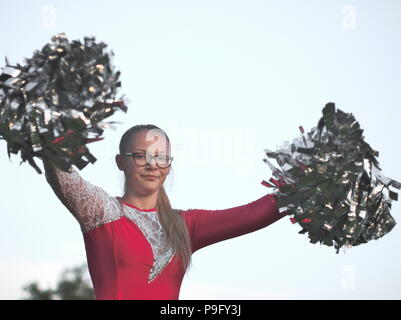 Bebrillter blonder Teen Majorette Mädchen mit Pom-poms Draußen im roten Kleid Stockfoto