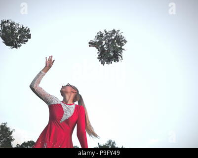 Bebrillter blonder Teen Majorette Mädchen mit Pom-poms Draußen im roten Kleid Stockfoto