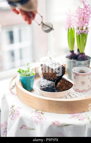 Chocolate Cupcake mit Zucker und Kaffee. Frühstück auf ein Tablett aus Holz und Blumen. Blick aus dem Fenster auf die Stadt Stockfoto