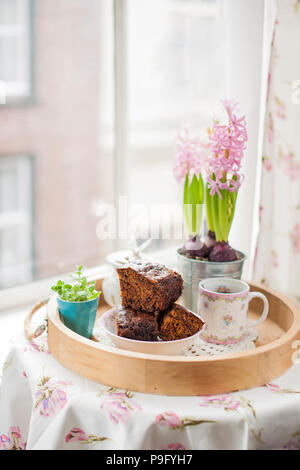 Chocolate Cupcake mit Zucker und Kaffee. Frühstück auf ein Tablett aus Holz und Blumen. Blick aus dem Fenster auf die Stadt. Stockfoto