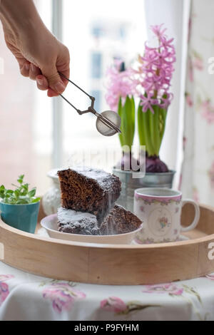 Chocolate Cupcake mit Zucker und Kaffee. Frühstück auf ein Tablett aus Holz und Blumen. Blick aus dem Fenster auf die Stadt Stockfoto
