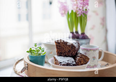 Chocolate Cupcake mit Zucker und Kaffee. Frühstück auf ein Tablett aus Holz und Blumen. Blick aus dem Fenster auf die Stadt. Stockfoto