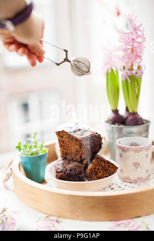 Chocolate Cupcake mit Zucker und Kaffee. Frühstück auf ein Tablett aus Holz und Blumen. Blick aus dem Fenster auf die Stadt. Freier Platz für Text oder eine Postkarte. Stockfoto