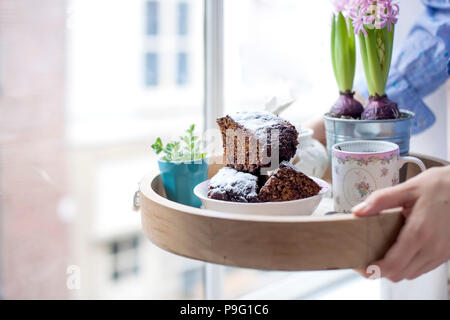 Chocolate Cupcake mit Zucker und Kaffee. Frühstück auf ein Tablett aus Holz und Blumen. Blick aus dem Fenster auf die Stadt. Freier Platz für Text oder eine Postkarte. Stockfoto