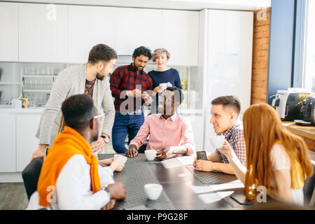 Junge aktive Menschen diskutieren ihre Startup Unternehmen am Tisch sitzen mit Tassen Kaffee Stockfoto