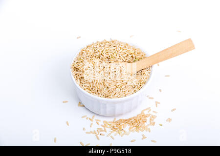 Nahrhafte, Whole-Grain brauner Reis in einer weißen Schüssel oder Ramekin auf weißem Hintergrund mit Holz Löffel Stockfoto