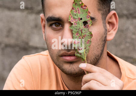 Ernsthafte junge Mann hält ein Blatt vor der Ruine und spähen durch die Bohrung Stockfoto