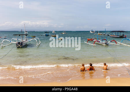 Traditionelle indonesische Outrigger Stil mit Fischerbooten (Jukung) und Baum Kinder in der Flut sitzen am Strand von Sanur, Bali, Indonesien. Stockfoto