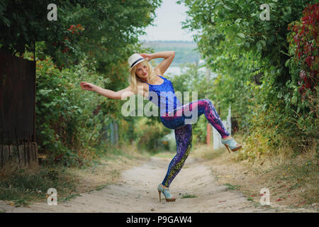 Junge lächelnde Mädchen in bunten Leggins, blau oben, weißen Hut und auf hohen Absätzen tanzen auf der Straße Stockfoto