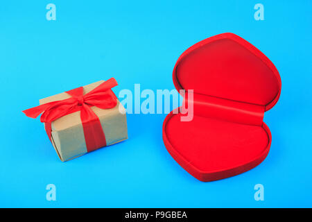 Leere helle rote Herzen Form Box und Geschenk verpackt mit roter Schleife auf blauem Hintergrund. Valentinstag, Liebe, Ehe Konzept Stockfoto