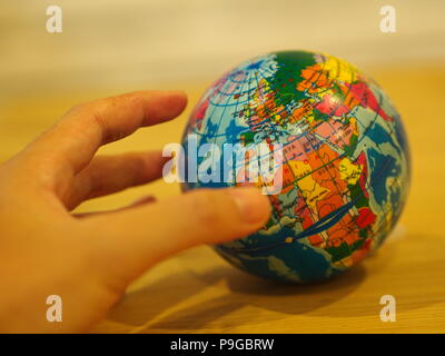 Nahaufnahme der Hand mit einem Mini Globus mit hölzernen Tisch Hintergrund Stockfoto