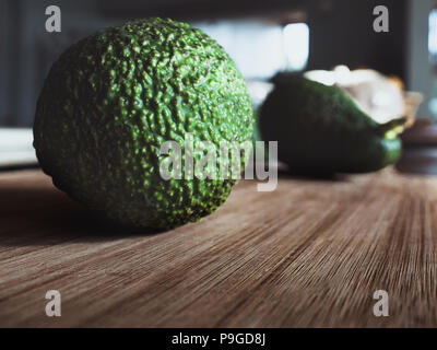 Avocado auf einem Holzbrett mit Küche und ein anderes Avocado im Hintergrund Stockfoto