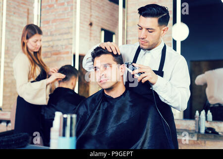 Professionelle friseur Mann tun Styling hübscher Kerl mit elektrischer Haarschneider bei Friseur Stockfoto