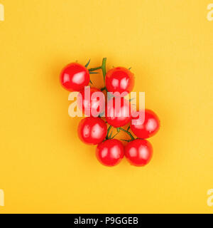 Bündel frische Kirschtomaten auf gelben Hintergrund. Ansicht von oben, minimale gestaltete Komposition. Stockfoto