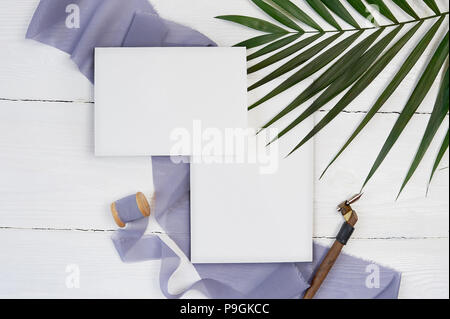 Weiße leere Grußkarte Band auf dem Hintergrund der blauen Stoff mit Palm Leaf und kalligraphischen Stift auf einem weißen Hintergrund. Mockup mit Umschlag und eine leere Karte. Flach. Ansicht von oben Stockfoto