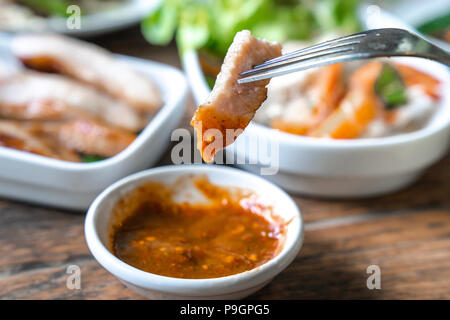 Nahaufnahme gegrillten Hals Schweinefleisch mit pikanter Sauce auf Gabel mit Nahrung und Holz- tabl Textur im Hintergrund, Holzkohle - gekochtes Schweinefleisch Hals. (Thai Stil Essen Stockfoto