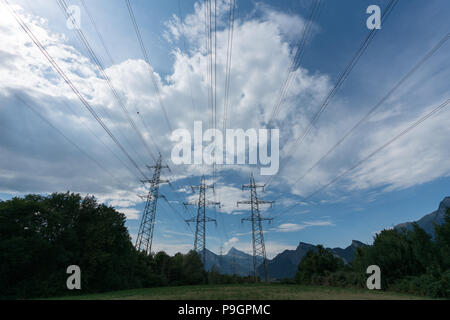 Freileitungen und Masten in Silhouette gegen einen blauen Himmel mit weißen Wolken und Bäume unterhalb Stockfoto