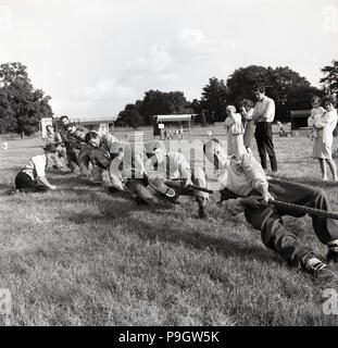 1967, historische, ein Team von männlichen Konkurrenten außerhalb in einem Feld ziehen, wie stark sie Teil kann in einem Tauziehen Konkurrenz an der Quainton Dorffest, Buckinghamshire, England, UK. Stockfoto