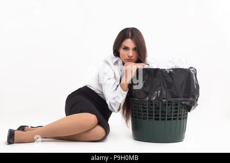 Mädchen sitzen neben dem Mülleimer auf ihn lehnend. Frau in Business Outfit sitzen auf dem Boden in Weiß studio lehnte sich auf Papierkorb standning Nächste Stockfoto