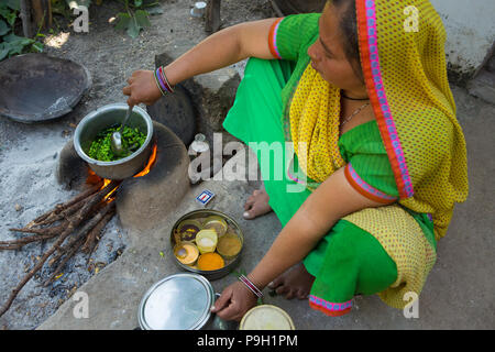 Eine Frau kochen Mittagessen außerhalb auf einem offenen Feuer an ihrem Haus in Ahmedabad, Indien. Stockfoto