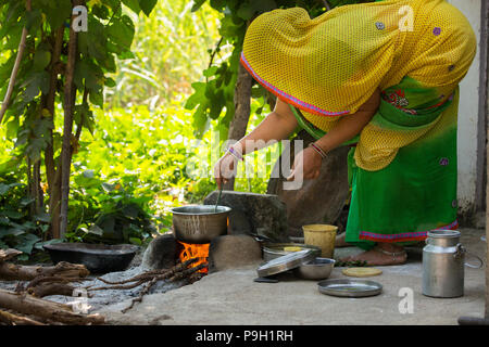 Eine Frau kochen Mittagessen außerhalb auf einem offenen Feuer an ihrem Haus in Ahmedabad, Indien. Stockfoto