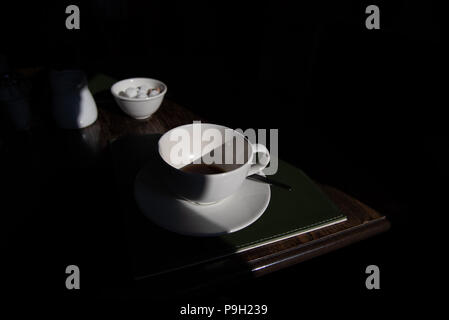 Eine weitere Tasse Kaffee für die Straße. Hoher Kontrast stimmungsvolles Bild. Hell erleuchtete leere Kaffeetasse und tiefen Schatten. Stockfoto