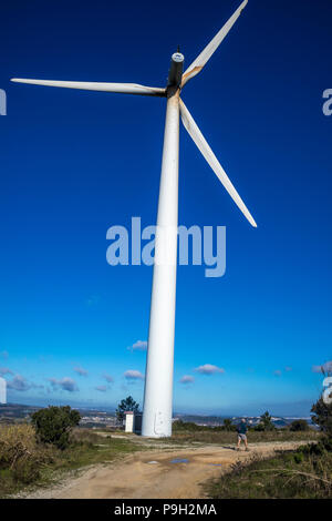 Ein einsamer Wanderer in der Region Leiria Portugal von einer riesigen windenergieanlage vor strahlend blauem Himmel in den Schatten gestellt Stockfoto