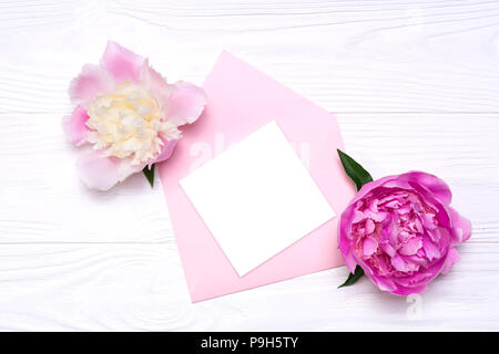 Eine leere Notiz auf ein rosa Umschlag. Zwei rosa Pfingstrose Blumen auf weißem Hintergrund Stockfoto