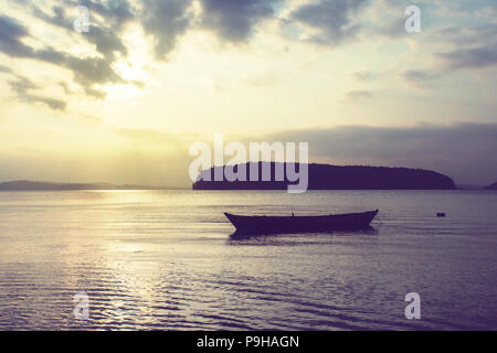 Holz- kleinen Boot auf dem Meer auf dem Hintergrund einer schönen Sonnenuntergang auf einem tropisch-exotischen Insel. Ein ruhiges Meer. Dorf Fischerboot in der indischen Provinz. Stockfoto