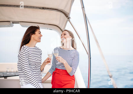 Zwei schöne europäische Mädchen mit langen Haaren, modisch gekleidet Toasten mit Gläsern Wein genießen Sie ein Meer Reise auf einem Schiff im Schwarzen Meer Stockfoto