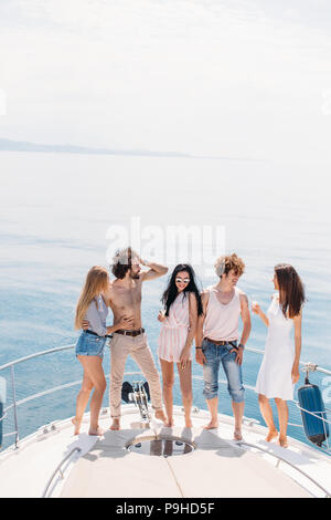 Luxus Urlaub. Freudige junge männliche und weibliche Freunde tanzen und Spaß auf einem Bug segeln Boot Deck, Lächeln, umarmen über amazing Blue Marine Stockfoto