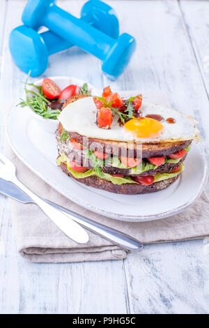 Toast von einem Korn Brot mit Käse und Tomaten und Ei. Vegetarisches Essen. auf einem weißen Teller und blau Hanteln für Fitness. Nützliche Frühstück. Freier Speicherplatz für das Schreiben von Text Stockfoto