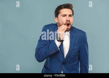 Gut gekleidete Geschäftsmann haben Schmerzen in den Zähnen. Portrait von Stattlichen bärtiger Mann im blauen Anzug und weißes Hemd, mit smart Watch. Innen- studio Shot, isol Stockfoto