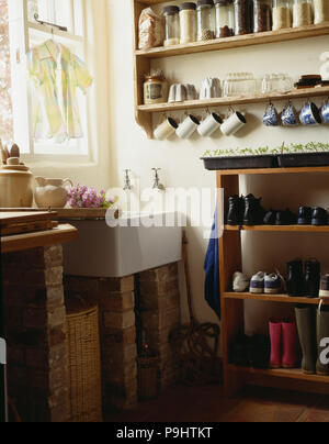 Storage jars auf Regalen vor weißen Waschbecken im rustikalen Hauswirtschaftsraum mit Schuhe auf den freistehenden hölzernen Regal gespeichert Stockfoto