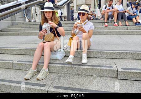 Zwei junge Frauen, die auf den Stufen auf dem Trafalgar Square beim Mittagessen sitzen, London, England, UK. Stockfoto