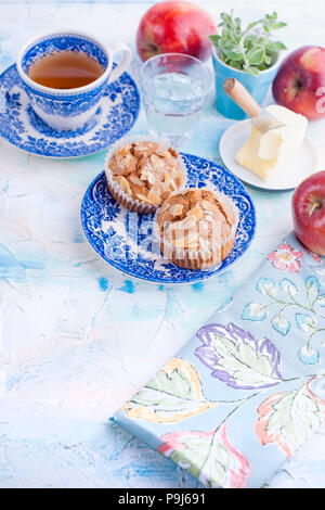 Hausgemachte Muffins mit Mandeln auf einem blauen Platte für Frühstück und Kaffee in eine Tasse. Ein Glas Wasser und ein Rot frischen Apfel und Butter für Sandwiches. Freier Platz für Text oder Postkarte Stockfoto