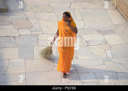 Eine attraktive indischen Frau in einem hellen orange Sari, Bürsten, die gepflasterte Fläche am Fort Amber Palast in Jaipur, Indien Stockfoto