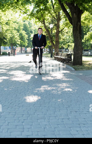 Geschäftsmann im Anzug ist Reiten auf einem Kick scooter im City Park Stockfoto
