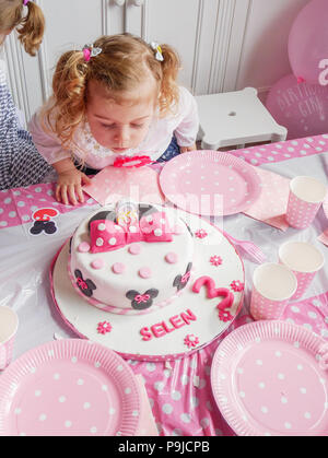 Drei Jahre alte Mädchen bläst die Kerzen auf dem Geburtstagskuchen, Großbritannien Stockfoto
