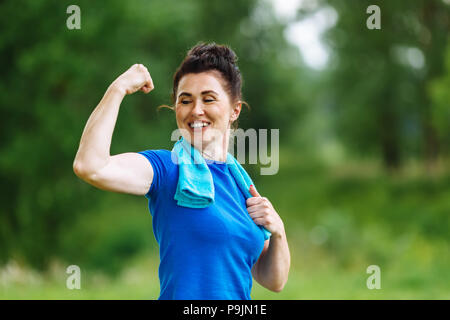 Lächelnd Senior Frau flexing Muskeln Outdoor im Park. Ältere Frauen zeigen Bizeps. Gesunden Lebensstil Konzept. Copyspace. Stockfoto