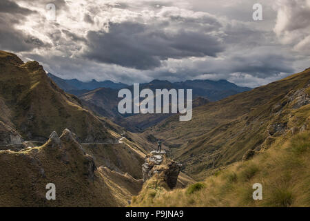 Wanderer steht auf einem Felsvorsprung ausgesetzt und blickt in Richtung Skippers Canyon, Queenstown, Otago, Südinsel, Neuseeland Stockfoto